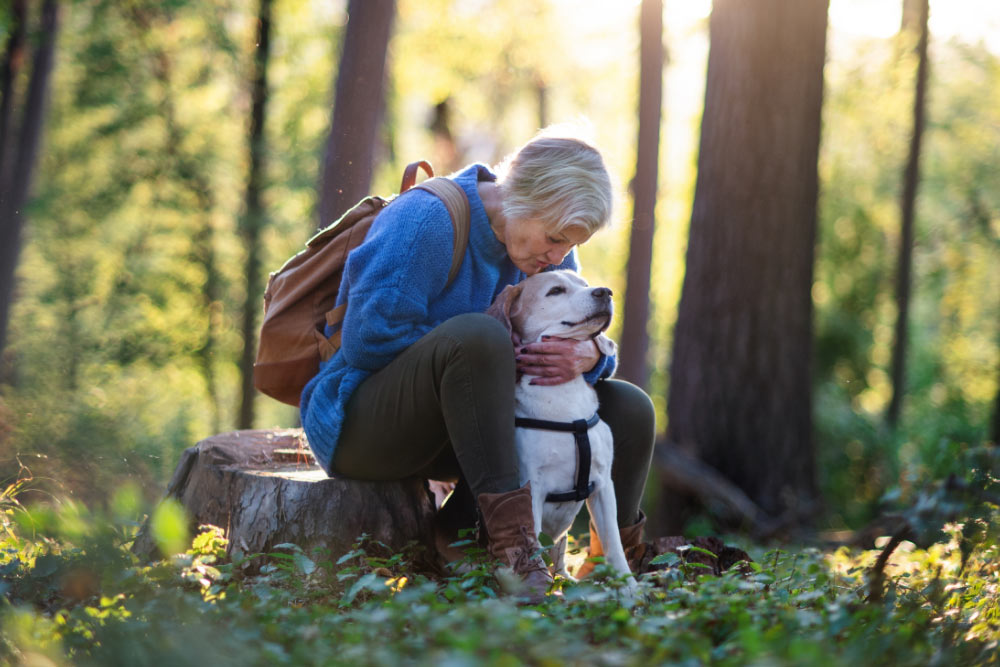 woman wearing a backpack sitting outside in nature with dog