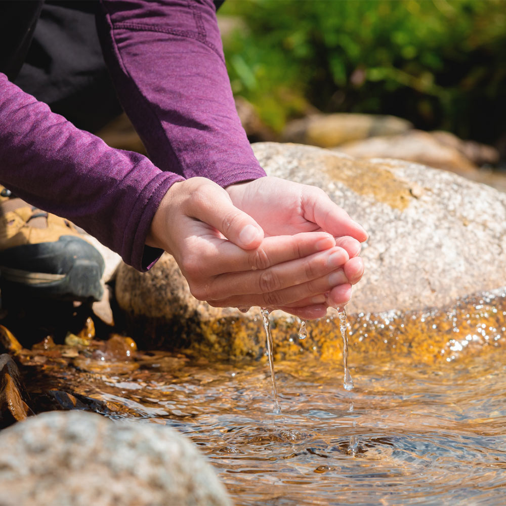 dlose-up of a woman's hand pouring water from her palms while trying to drink from a clean water source in nature